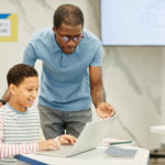 Bild einer Lehrkraft, die mit einem Schüler im Klassenzimmer arbeitet und dabei computergestützte Instrumente zur formativen Beurteilung einsetzt