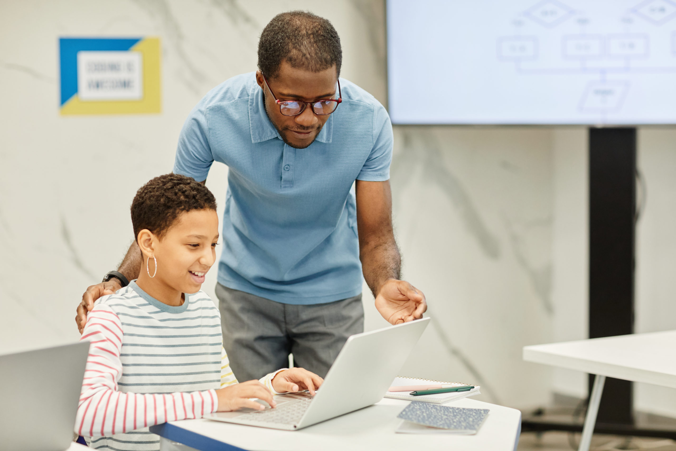 Bild einer Lehrkraft, die mit einem Schüler im Klassenzimmer arbeitet und dabei computergestützte Instrumente zur formativen Beurteilung einsetzt