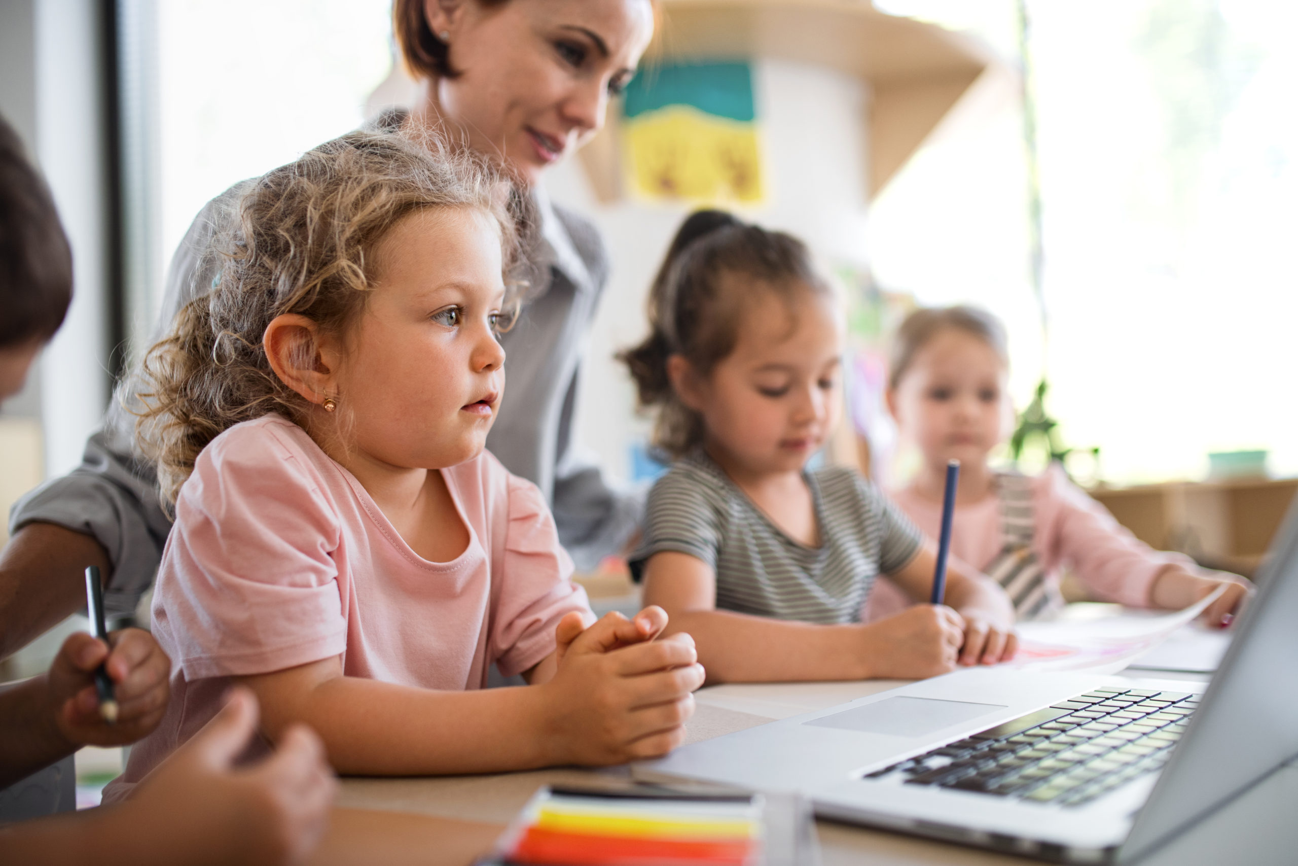 コンピュータを使った幼児教育に参加する先生と生徒の写真。