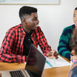 Estudiantes multirraciales utilizan un ordenador portátil para investigar sobre un proyecto mientras estudian juntos en la escuela.