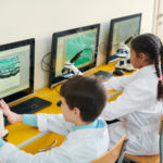Group of contemporary schoolchildren sitting in front of computer displays and participating in a a game-based science lesson