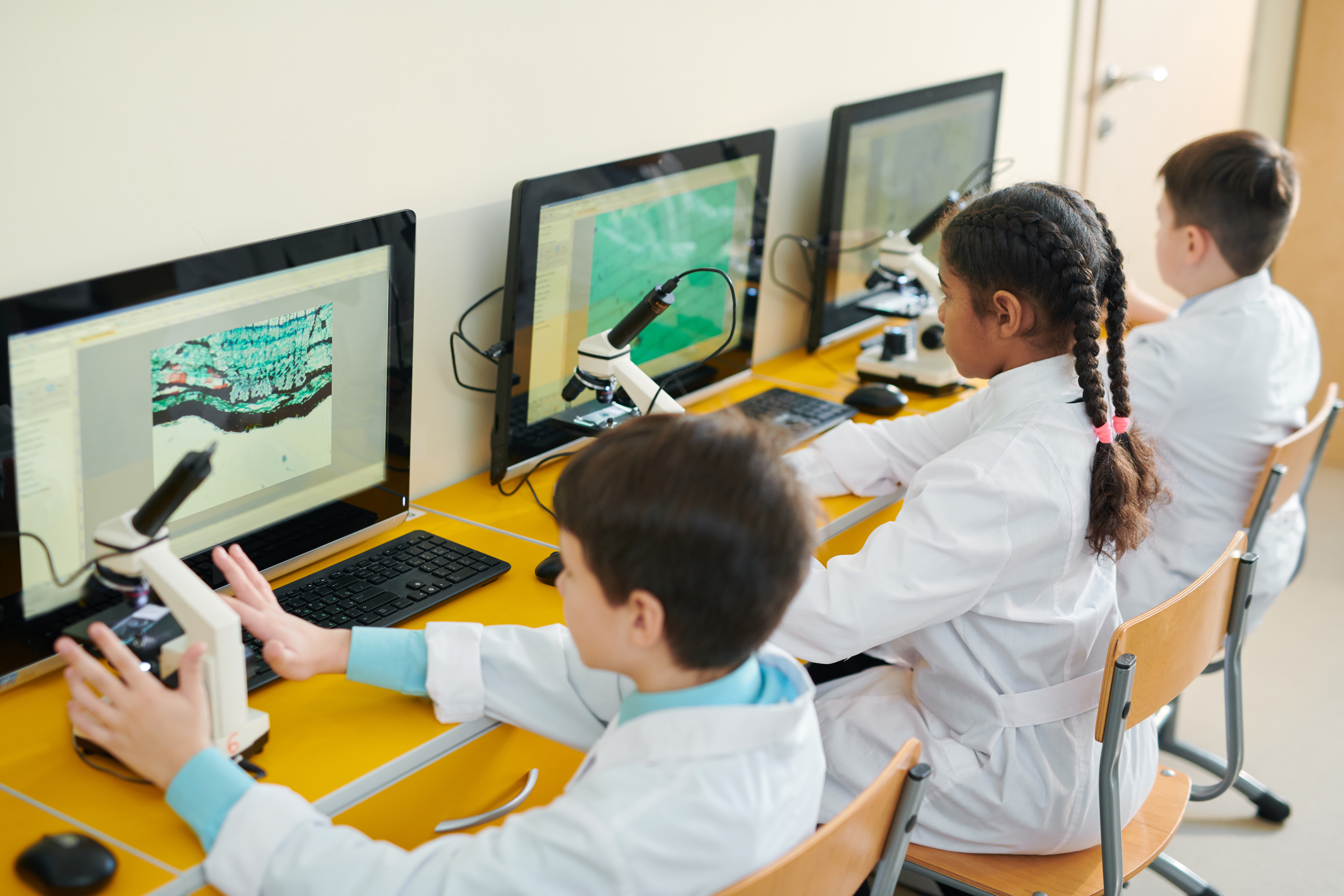 Groupe d'écoliers contemporains assis devant des écrans d'ordinateur et participant à une leçon de science basée sur un jeu.