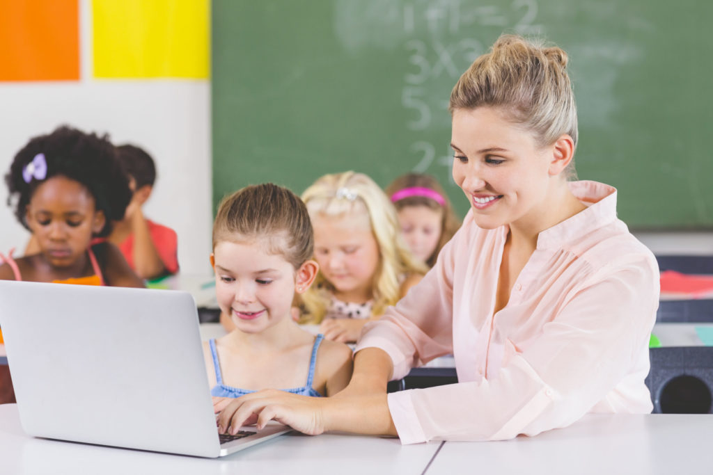 ノートパソコンで女子生徒を教える女性教師