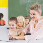 Female teacher teaching schoolgirl on laptop