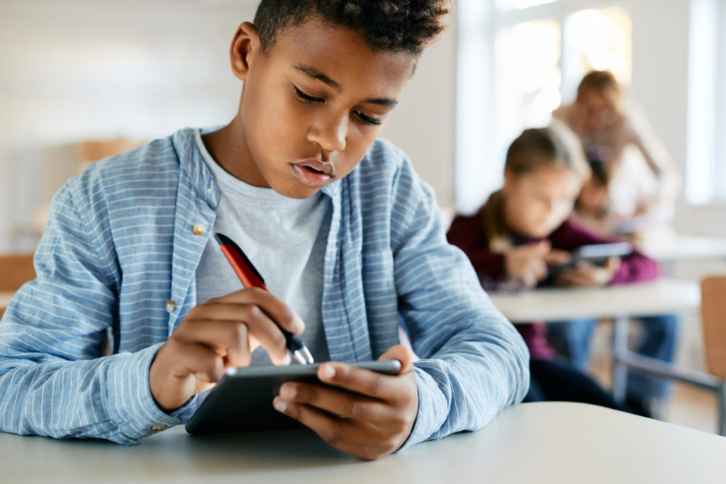 Ein junger Schüler benutzt ein digitales Tablet, um während einer Unterrichtsstunde im Klassenzimmer mit einer spielerischen Bewertung zu interagieren.