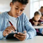 Joven escolar utilizando una tableta digital para interactuar con una evaluación gamificada durante una clase en el aula.