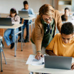 学校のコンピュータの授業で、小学生のノートパソコンの使い方をサポートする熟年教師。