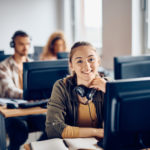Joven mujer feliz asistiendo a clase de informática en la universidad y mirando a cámara.