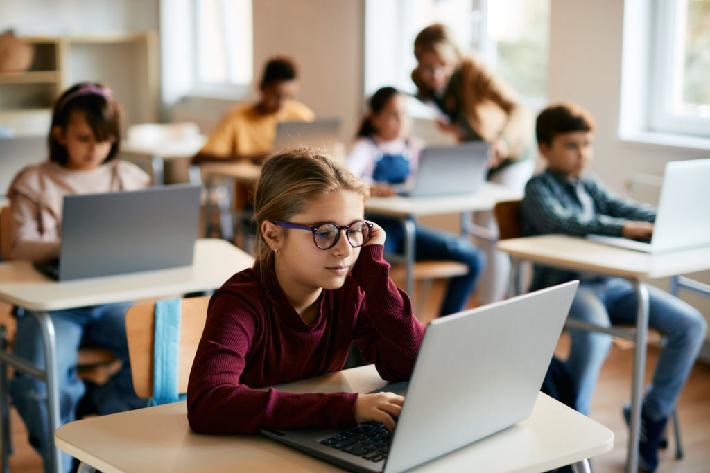 小学校のコンピュータの授業で、ノートパソコンを使って評価を受ける女子児童。