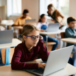 Une écolière utilise un ordinateur portable pendant un cours d'informatique pour passer une évaluation à l'école primaire.