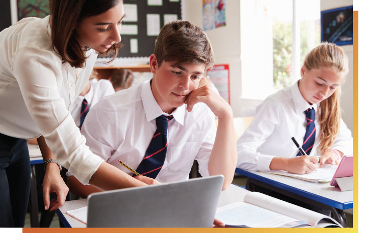 Female teacher leaning over to help student sitting at a computer