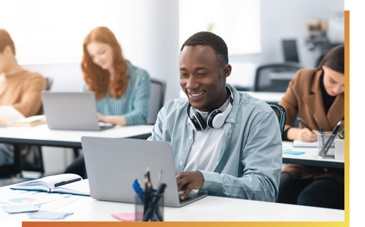 Internationale Studierende sitzen an Schreibtischen und benutzen Laptops.