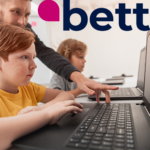 children sitting at computers with an older man behind pointing at the screen.