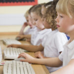 side view of young girl working at a computer using a technology based assessment system for secure K-12 testing.