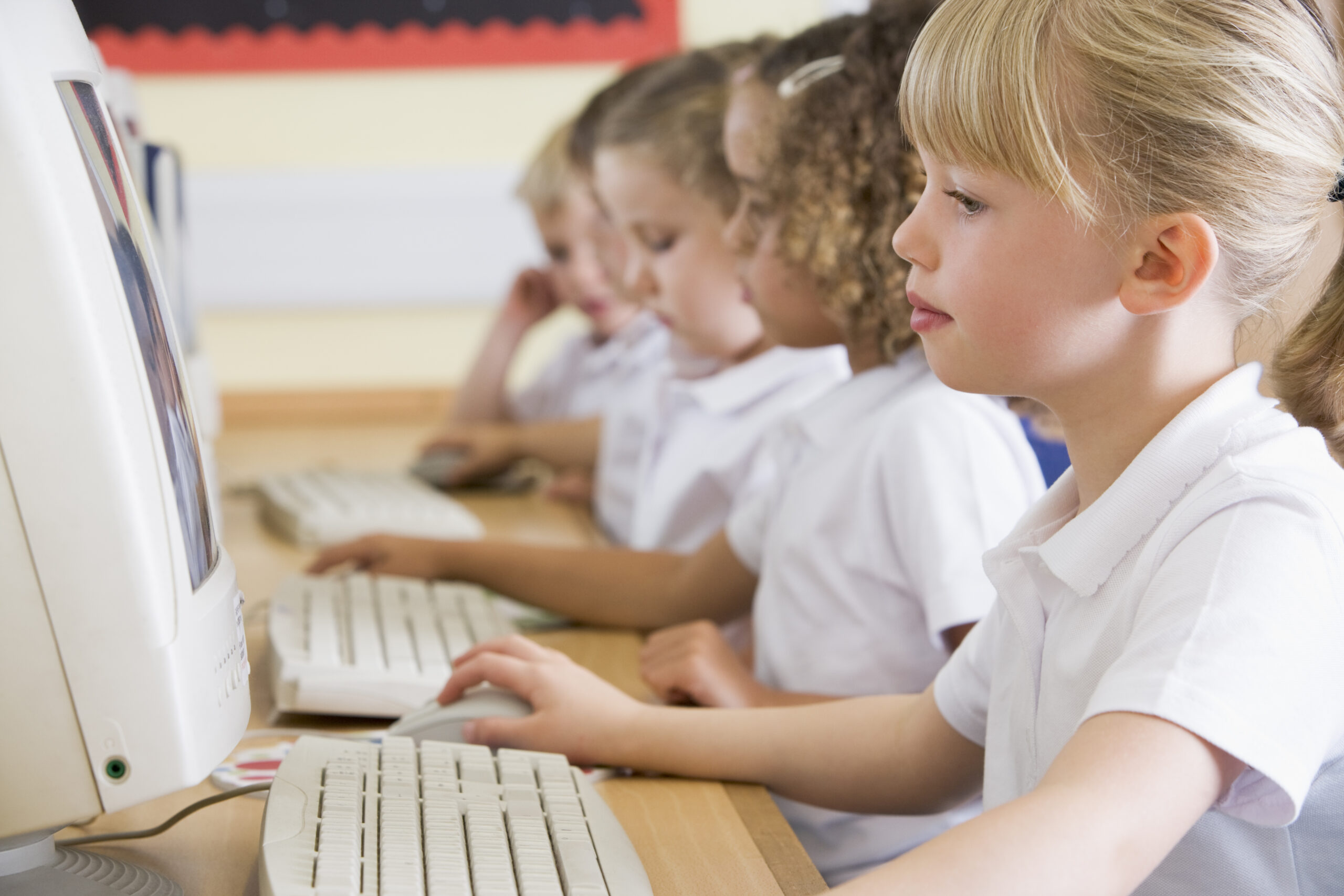 side view of young girl working at a computer using a technology based assessment system for secure K-12 testing.