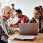 ノートパソコンの画面を見ている2人の女子学生をクローズアップし、背景の他の学生にはピントを合わせず、創造的な評価のアイデアを示す。