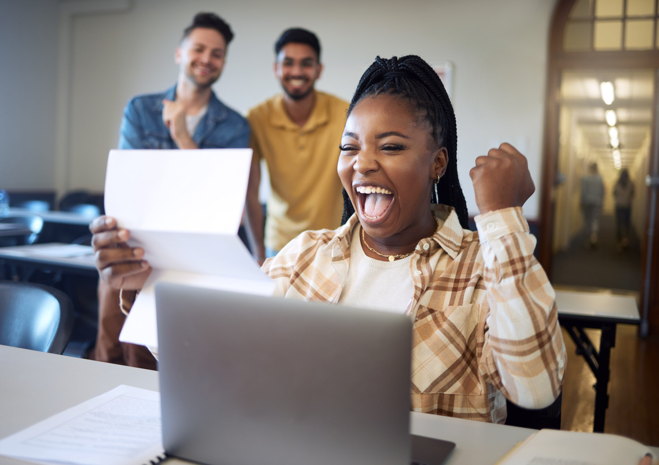 Estudiante universitaria sonriente y animada delante de su ordenador tras recibir los resultados de una herramienta de evaluación formativa en línea.