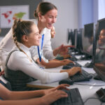 Gruppe von Sekundarschülern an Computern im IT-Unterricht mit einer Lehrerin, die das Konzept des adaptiven Lernens demonstriert