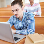 Un étudiant d'âge universitaire assis dans un amphithéâtre en train de passer une évaluation sommative sur son ordinateur portable.