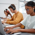 Vue de côté de trois étudiants assis en rang devant leur ordinateur et portant des écouteurs, en train de passer une évaluation en ligne.