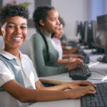 Des enfants assis devant des ordinateurs dans une salle de classe, soulignant les avantages des tests informatisés et des examens informatisés.