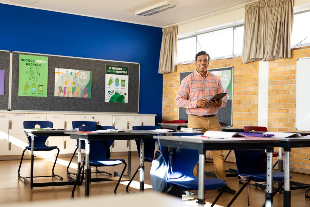 Lehrer, der in einem leeren Klassenzimmer steht und ein Tablet in der Hand hält, um das Konzept der Erstellung eines Lehrplan-Leitfadens zu erläutern
