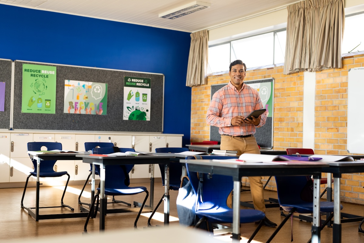 Profesor de pie en un aula vacía sosteniendo una tableta, mostrando el concepto de creación de una guía de ritmo curricular.