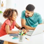 father and daughter having fun doing homework with laptop at home