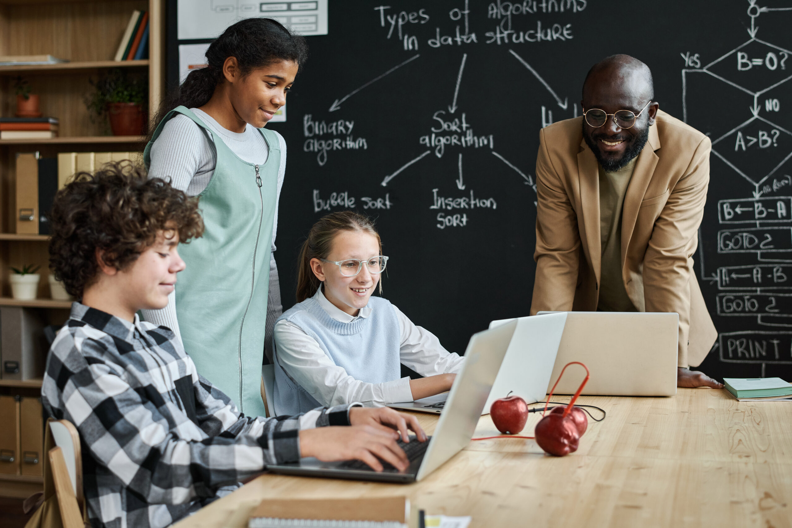 Group of children learning to work with computer program using laptop computers at table together with teacher at lesson in a flipped classroom model