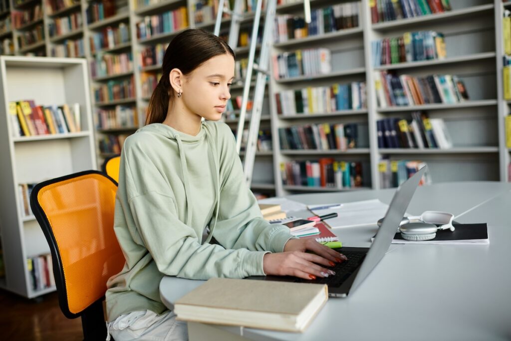 Teenage female student studying on her laptop while sitting in a library, showing the concept of schools adopting blended learning strategies.