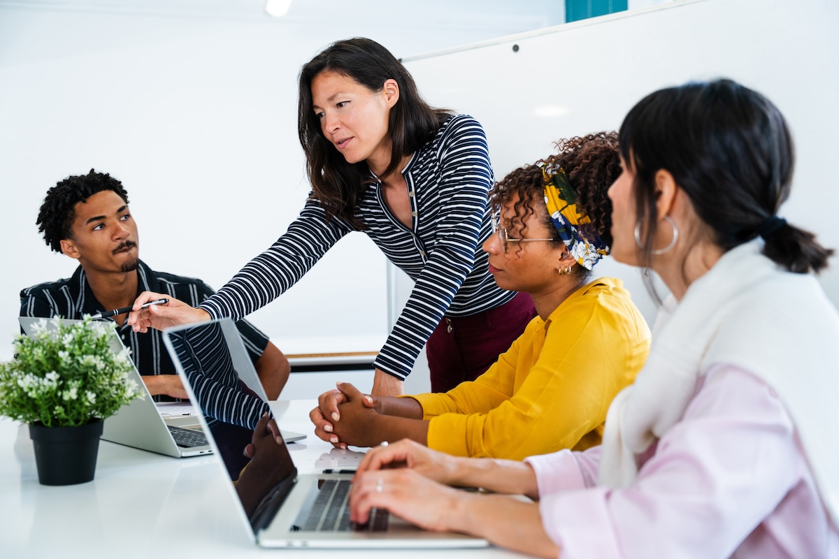 Four professionals working together using laptops with one woman pointing at the laptop screen as they research open educational resources examples.
