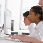 Side view of two female students and one male student sitting in a row in a computer class while looking at their desktop computers, showing the use of open educational resources in a school context.