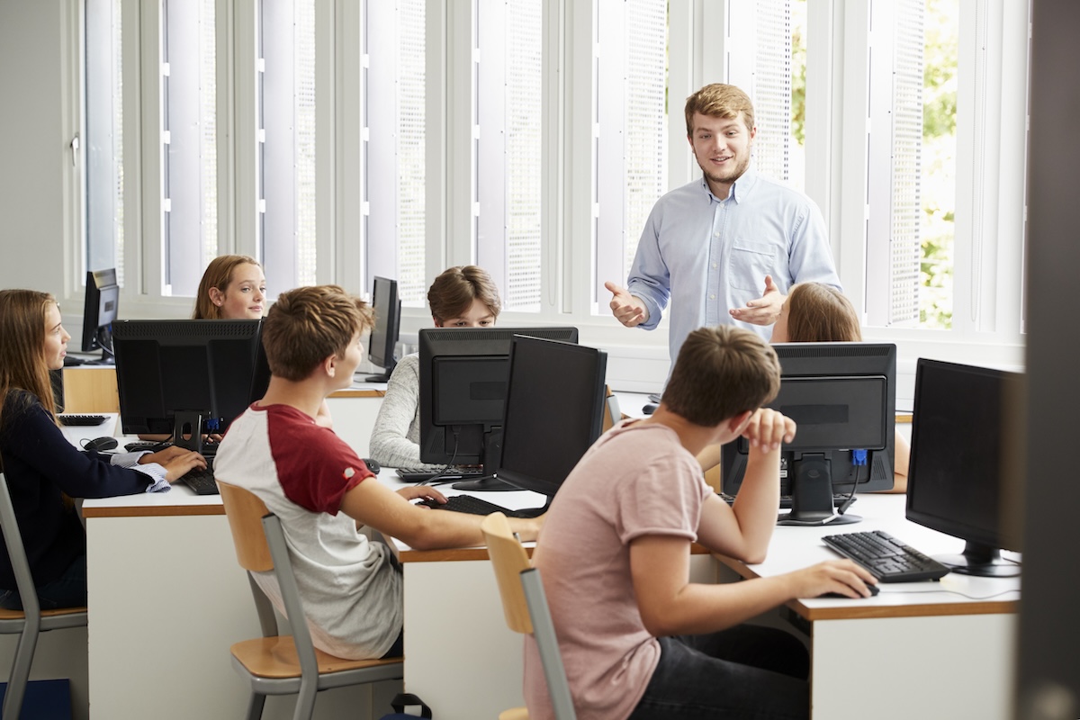 Teacher guiding students during a hands-on computer class, demonstrating educational best practices in a collaborative learning environment.