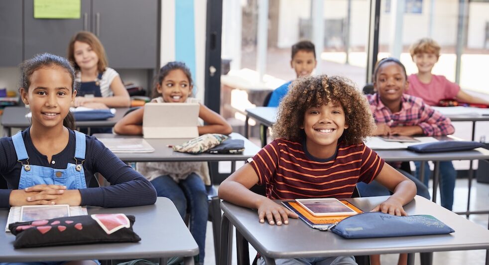 Portrait of elementary school pupils sitting at their desks preparing to take an assessment in a modern K-12 classroom setting