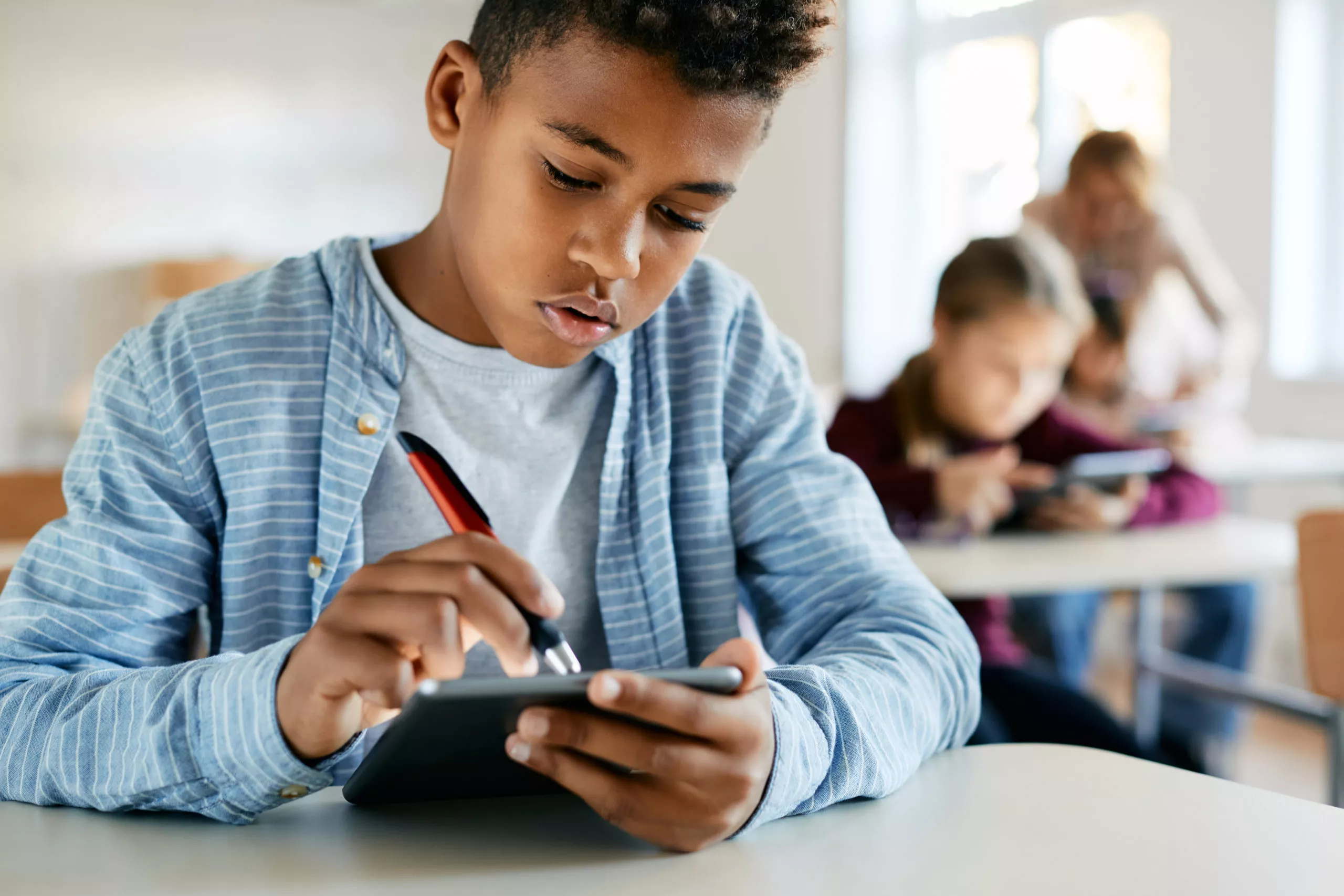 Young schoolboy using a digital tablet to interact with a gamified assessmentduring a class in the classroom.