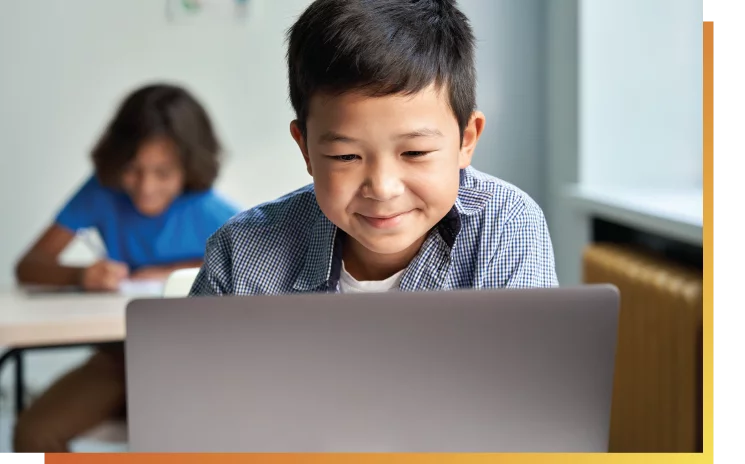 smiling young boy sitting in front of laptop looking down