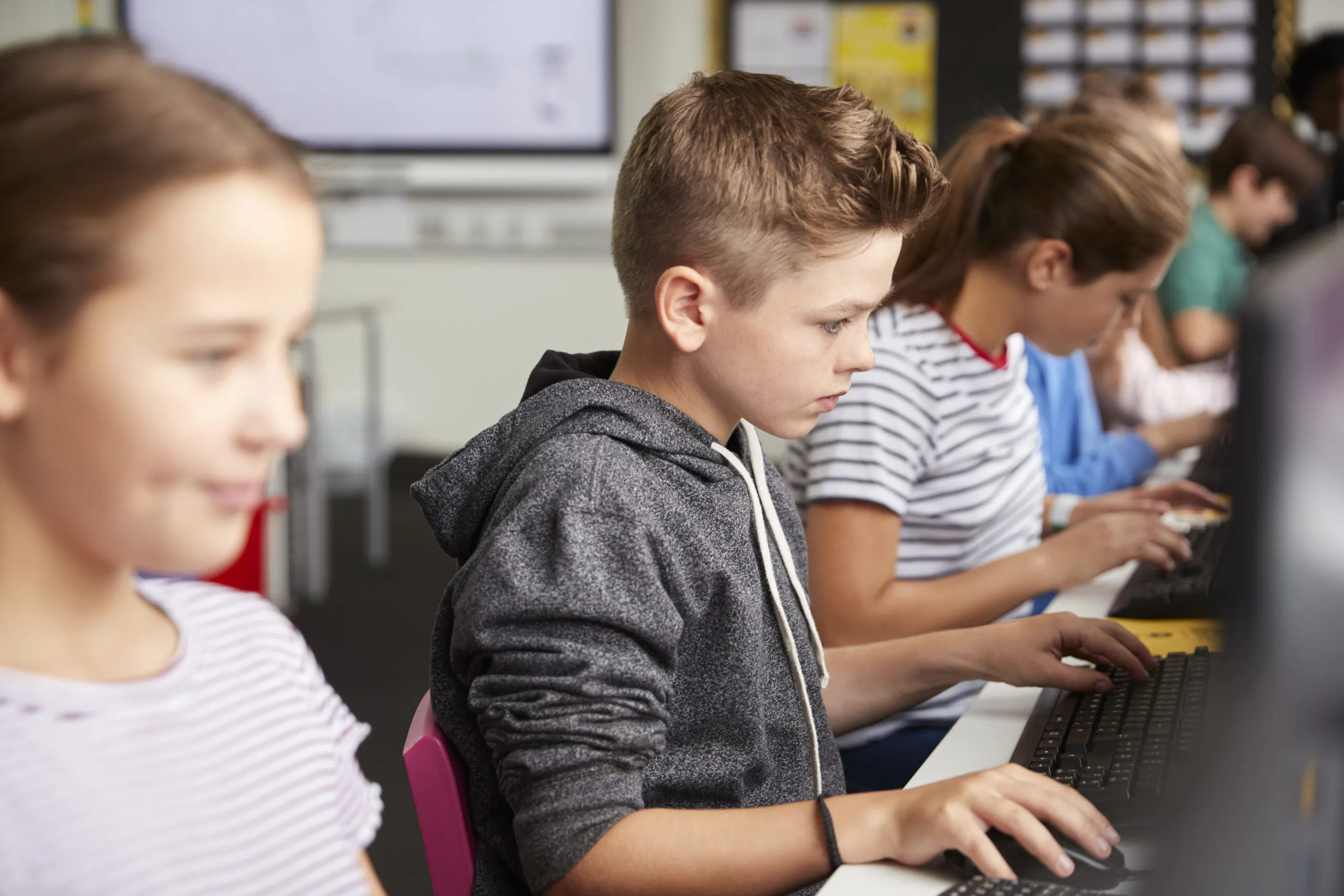 side view of a line of male and female students sitting at computers using standardized assessment tools.