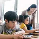 young boy, girl and teacher using computers computer in primary school classroom. Showing the concept of overcoming assessment challenges.