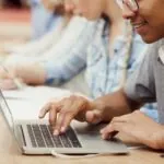 male student wearing headphones and typing on a laptop taking a subjective essay-based assessment