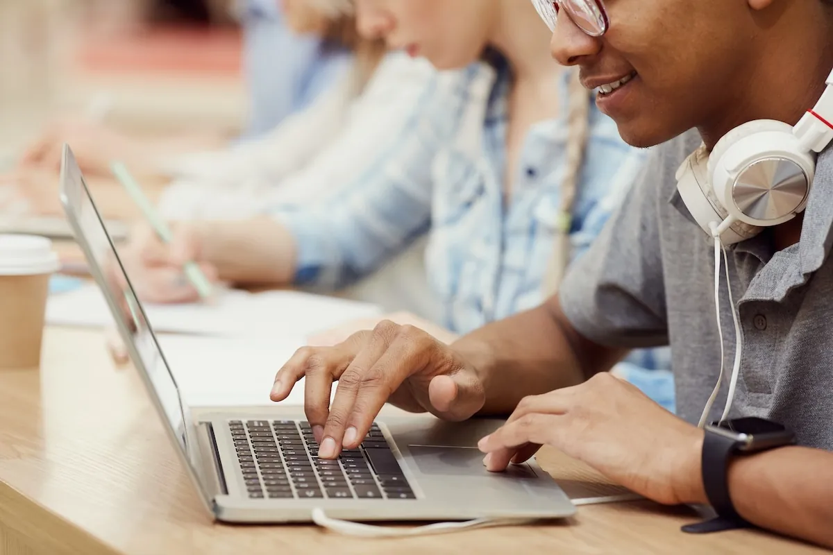 male student wearing headphones and typing on a laptop taking a subjective essay-based assessment