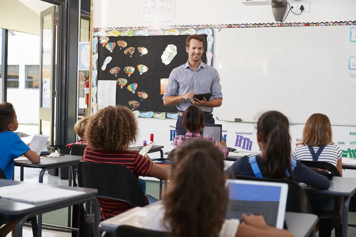 Male teacher standing in front of a classroom reviewing students progress.