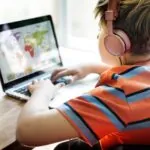 Boy wearing headphones sitting at a desk playing a game on his laptop highlighting the concept of visual learning strategies