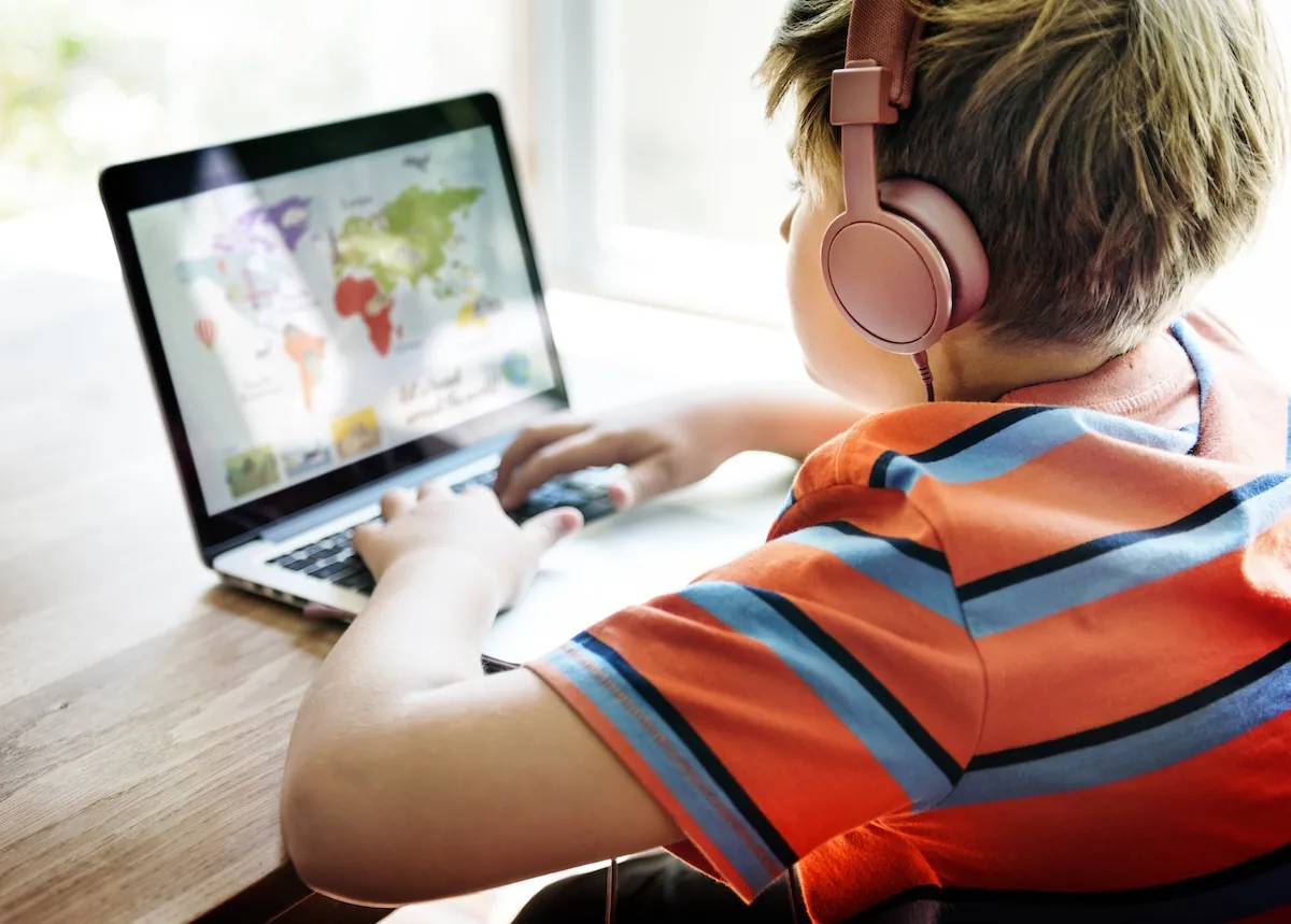 Boy wearing headphones sitting at a desk playing a game on his laptop highlighting the concept of visual learning strategies