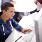 Teenage male student sitting in front of a computer typing on a keyboard, showing the concept of how to study for a test.