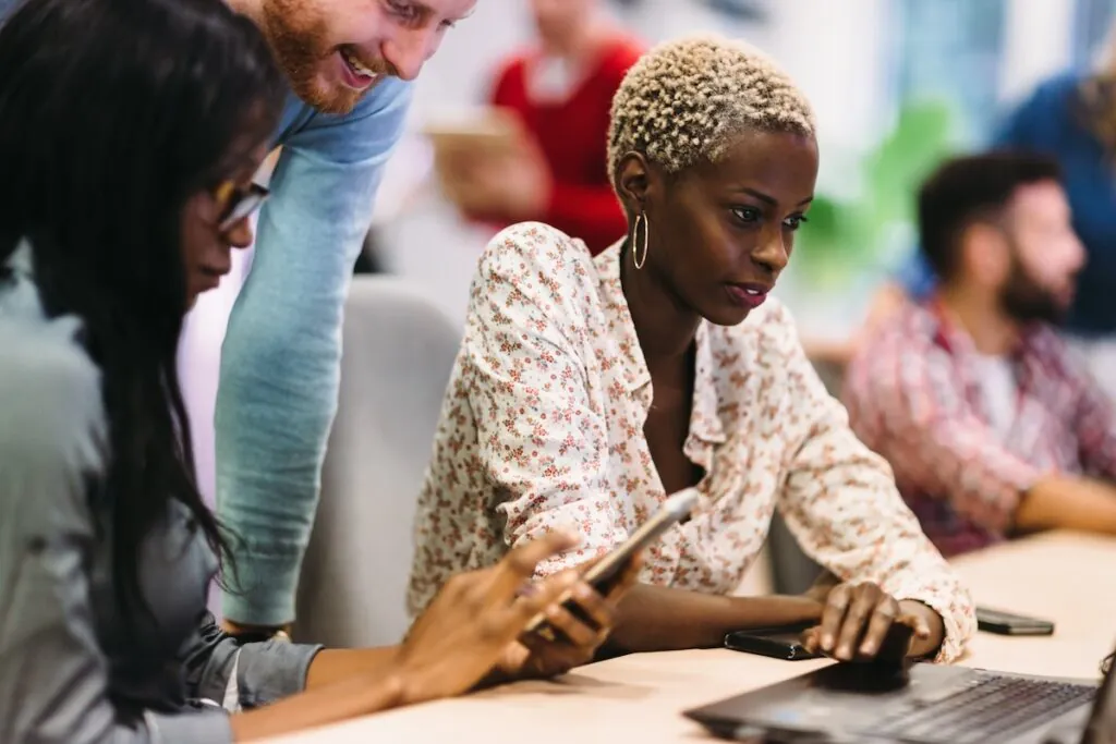 two women and a man leaning over a computer, demonstrating the concept of using open source tools to work on a project.
