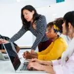 Four professionals working together using laptops with one woman pointing at the laptop screen as they research open educational resources examples.
