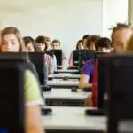 Room of students sitting in a computer lab while each student looks at their desktop monitor, demonstrating a practical application of open source exam management tools in an educational setting