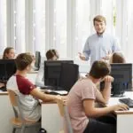 Enseignant guidant ses élèves pendant un cours pratique d'informatique, illustrant les meilleures pratiques pédagogiques dans un environnement d'apprentissage collaboratif.