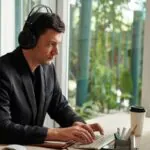 Male assessment candidate is wearing headphones and sitting at a desktop computer while taking a digital government recruitment exam.