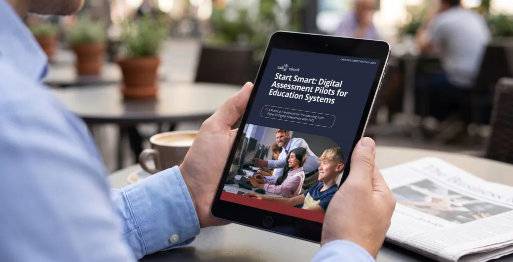 Photo en gros plan d'une personne vêtue d'une chemise bleue boutonnée, tenant une tablette dans un café bien éclairé. L'écran de la tablette affiche le titre « Start Smart : projets pilotes d'évaluation numérique pour les systèmes éducatifs ».